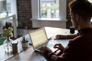 Man werkt op een laptop aan een bureau bij het raam
