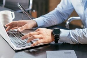 Handen typen op een laptop naast een kop koffie